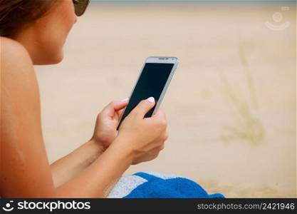 Communication concept. Young woman spending time on summer beach texting messages on smartphone. Girl using mobile phone.. Woman on beach texting on smartphone.