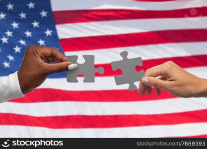 communication, cooperation and people concept - black and white hands matching pieces of puzzle over flag of united states background. black and white hands matching pieces of puzzle