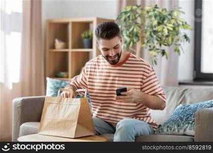 communication, leisure and people concept - happy smiling man using smartphone for takeaway food order check up at home. man with phone checking food order at home