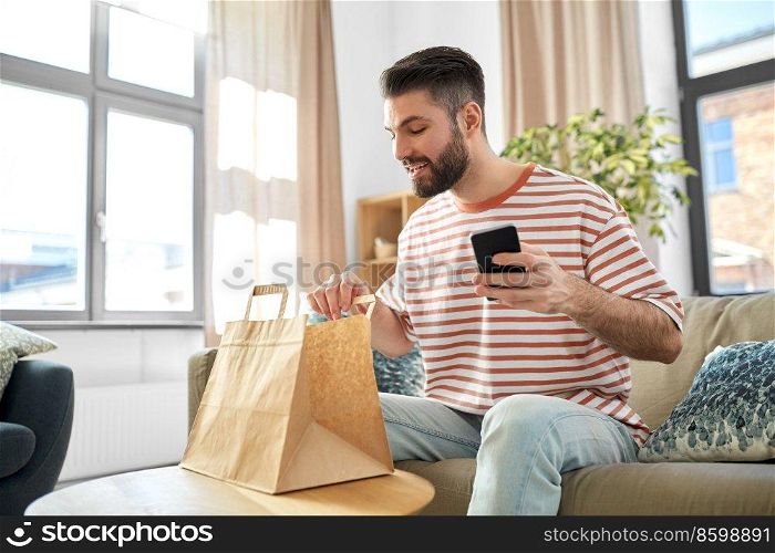 communication, leisure and people concept - man using smartphone for takeaway food order check up at home. man with phone checking food order at home