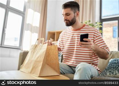 communication, leisure and people concept - man using smartphone for takeaway food order check up at home. man with phone checking food order at home