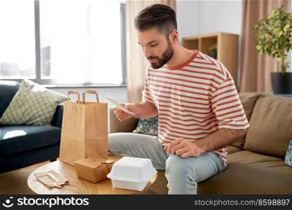 communication, leisure and people concept - man with bill checking takeaway food order at home. man with bill checking takeaway food order at home