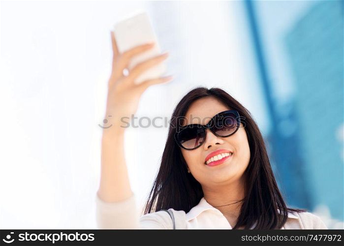 communication, lifestyle and technology concept - smiling young asian woman taking selfie by smartphone on city street. asian woman taking selfie by smartphone in city
