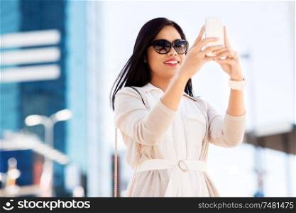 communication, lifestyle and technology concept - smiling young asian woman taking selfie by smartphone on city street. asian woman taking selfie by smartphone in city