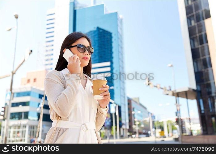 communication, lifestyle and technology concept - young asian woman in sunglasses with takeaway coffee cup calling on smartphone on city street. asian woman calling on smartphone in city