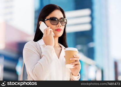communication, lifestyle and technology concept - young asian woman in sunglasses with takeaway coffee cup calling on smartphone on city street. asian woman calling on smartphone in city