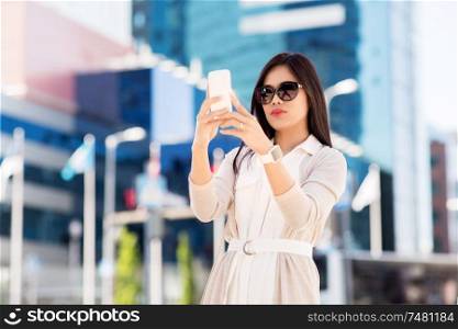 communication, lifestyle and technology concept - young asian woman taking selfie by smartphone on city street. asian woman taking selfie by smartphone in city