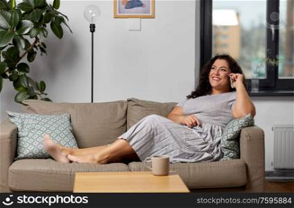 communication, people and leisure concept - happy young woman calling on smartphone on sofa at home. happy young woman calling on smartphone at home
