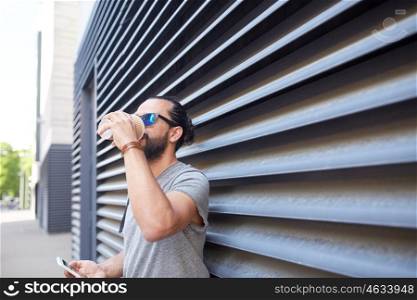 communication, technology and people concept - close up of man with smartphone drinking coffee from disposable paper cup on city street