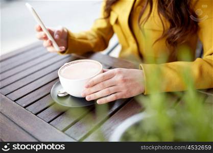 communication, technology, leisure and people concept - close up of young woman or teenage girl texting on smartphone and drinking cocoa at city street cafe terrace
