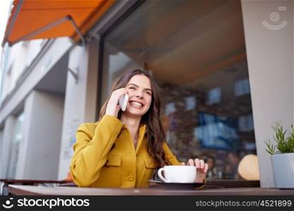 communication, technology, leisure and people concept - happy young woman or teenage girl calling on smartphone and drinking cocoa at city street cafe terrace