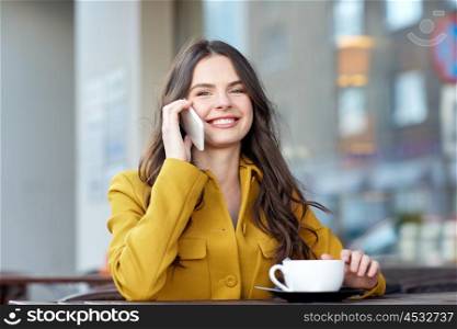 communication, technology, leisure and people concept - happy young woman or teenage girl calling on smartphone and drinking cocoa at city street cafe terrace