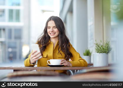 communication, technology, leisure and people concept - happy young woman or teenage girl texting on smartphone and drinking cocoa at city street cafe terrace