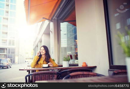 communication, technology, leisure and people concept - happy young woman or teenage girl calling on smartphone and drinking cocoa at city street cafe terrace. happy woman calling on smartphone at city cafe