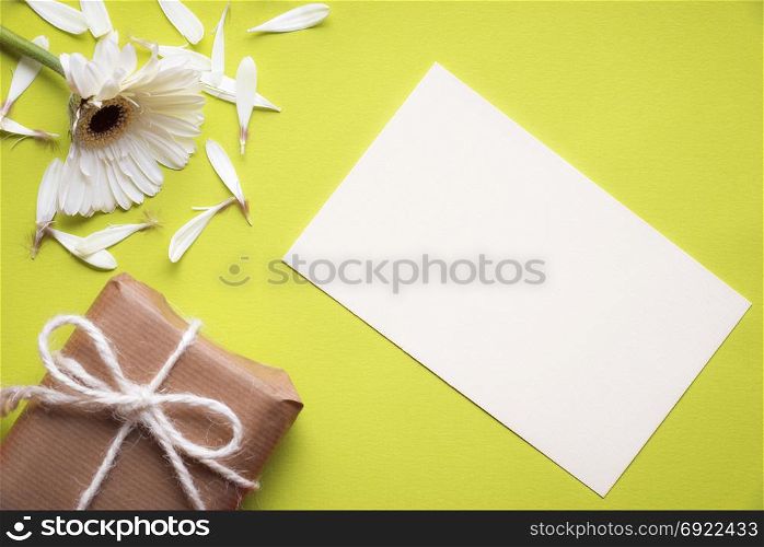 Communication theme image with a blank paper note, a torn white chrysanthemum flower and a gift box wrapped in vintage brown paper, on a yellow paper background.