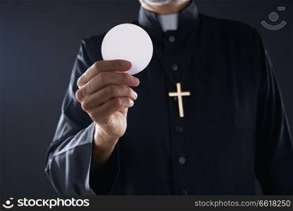 Communion wafer hostia priest in hands with cross