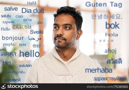communivation, translation and international concept - indian man in knitted woolen sweater at office over greeting words in different foreign languages. indian man over words in foreign languages