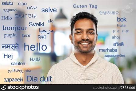 communivation, translation and international concept - smiling indian man in knitted woolen sweater at office over greeting words in different foreign languages. indian man over words in foreign languages