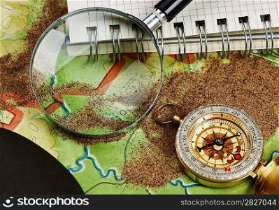 compass and notebook on the map with sand