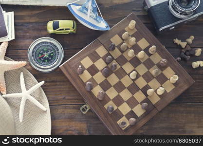 compass, chessboard, hat, passport, banknote money, camera, map, car ship and starfish figurine on wooden table for use as traveling concept (vintage tone and selected focus)