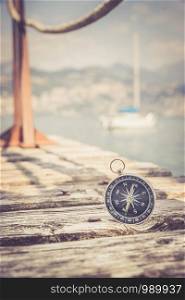 Compass lying on wooden dock pier in the foreground, sailing boats in the blurry background