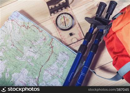 compass, map, trekking poles and backpack on a wooden background