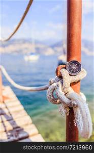 Compass on a lying on a sailing rope, ocean and sailing boats in the blurry background