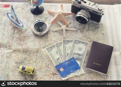 compass, passport, credit card, banknote money, globe, camera, map, car ship and starfish figurine on wooden table for use as traveling concept (vintage tone and selected focus)