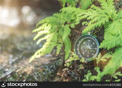 Compass put on the rock with green plant near waterfall with sunlight. Travel concept.
