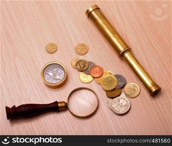 compass, telescope, magnifier and coin on a wooden table. compass, telescope, magnifier and coin