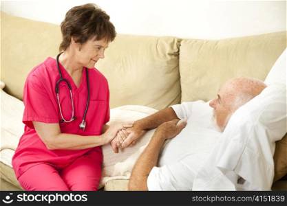 Compassionate home health nurse holds an elderly patient&rsquo;s hand.