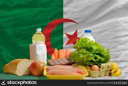 complete national flag of algeria covers whole frame, waved, crunched and very natural looking. In front plan are fundamental food ingredients for consumers, symbolizing consumerism an human needs