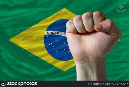 complete national flag of brazil covers whole frame, waved, crunched and very natural looking. In front plan is clenched fist symbolizing determination