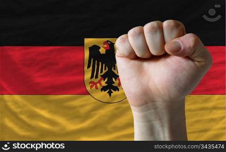 complete national flag of germany covers whole frame, waved, crunched and very natural looking. In front plan is clenched fist symbolizing determination
