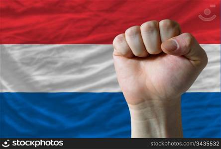 complete national flag of netherlands covers whole frame, waved, crunched and very natural looking. In front plan is clenched fist symbolizing determination