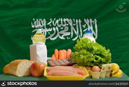complete national flag of saudi arabia covers whole frame, waved, crunched and very natural looking. In front plan are fundamental food ingredients for consumers, symbolizing consumerism an human needs
