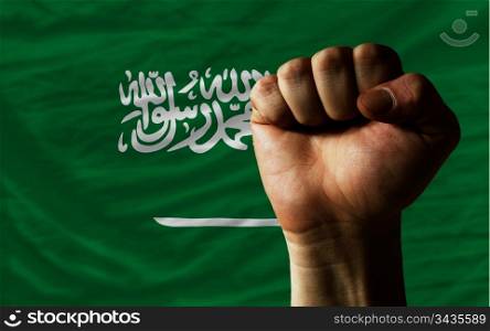 complete national flag of saudi arabia covers whole frame, waved, crunched and very natural looking. In front plan is clenched fist symbolizing determination