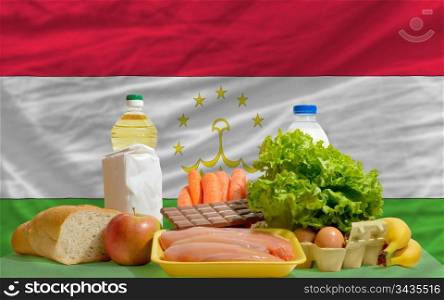 complete national flag of tajikistan covers whole frame, waved, crunched and very natural looking. In front plan are fundamental food ingredients for consumers, symbolizing consumerism an human needs