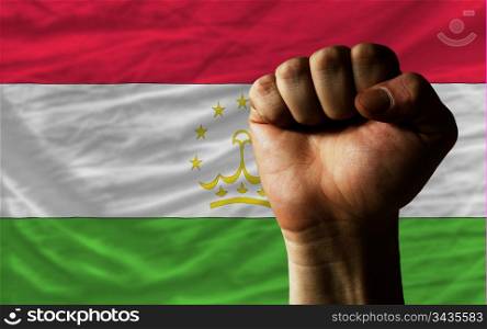 complete national flag of tajikistan covers whole frame, waved, crunched and very natural looking. In front plan is clenched fist symbolizing determination