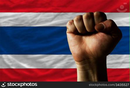 complete national flag of thailand covers whole frame, waved, crunched and very natural looking. In front plan is clenched fist symbolizing determination