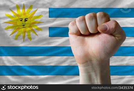 complete national flag of uruguay covers whole frame, waved, crunched and very natural looking. In front plan is clenched fist symbolizing determination