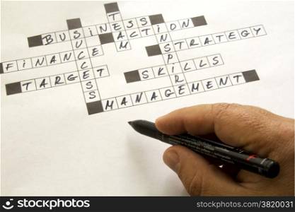completed business crossword and hand with pen