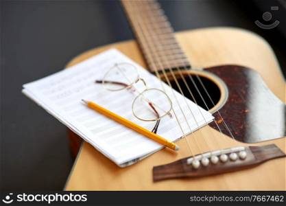 composing and music writing concept - close up of acoustic guitar with music book, pencil and glasses. close up of guitar, music book, pencil and glasses