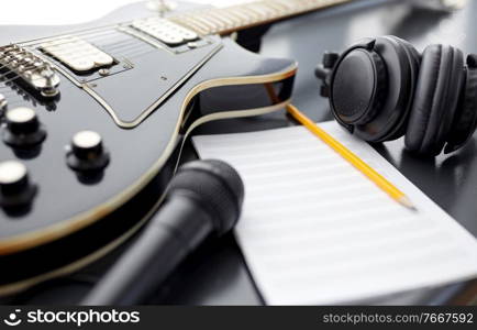 composing and music writing concept - close up of bass guitar with music book, microphone and headphones on black table. close up of guitar, music book and headphones