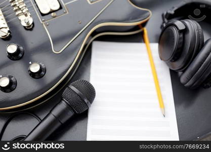 composing and music writing concept - close up of bass guitar with music book, microphone and headphones on black table. close up of guitar, music book and headphones