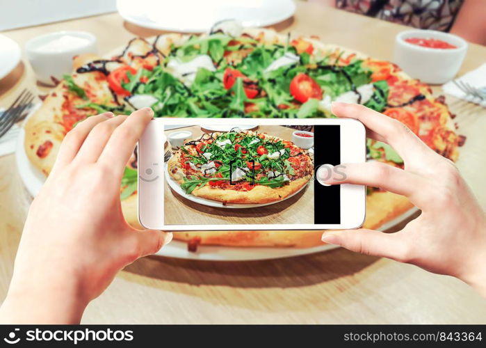 Composite image of making pizza photos on a smartphone - woman's hands holding mobile phone and touching shutter button on the screen.