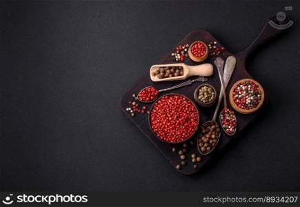 Composition, concept, consisting of several types of different colors of allspice in bowls and spoons on a dark concrete background