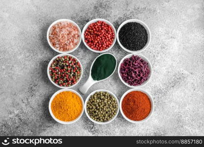 Composition consisting of a variation of several types of spices in white ceramic bowls on a textured concrete background