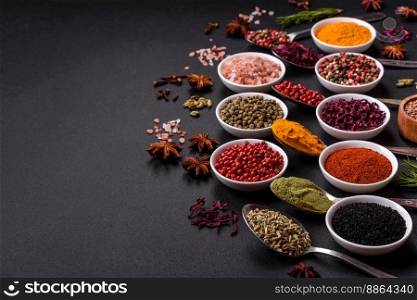 Composition consisting of variations of spices in white bowls and metal spoons on a dark concrete background