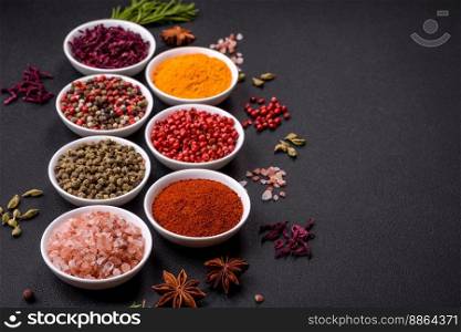 Composition consisting of variations of spices in white bowls and metal spoons on a dark concrete background